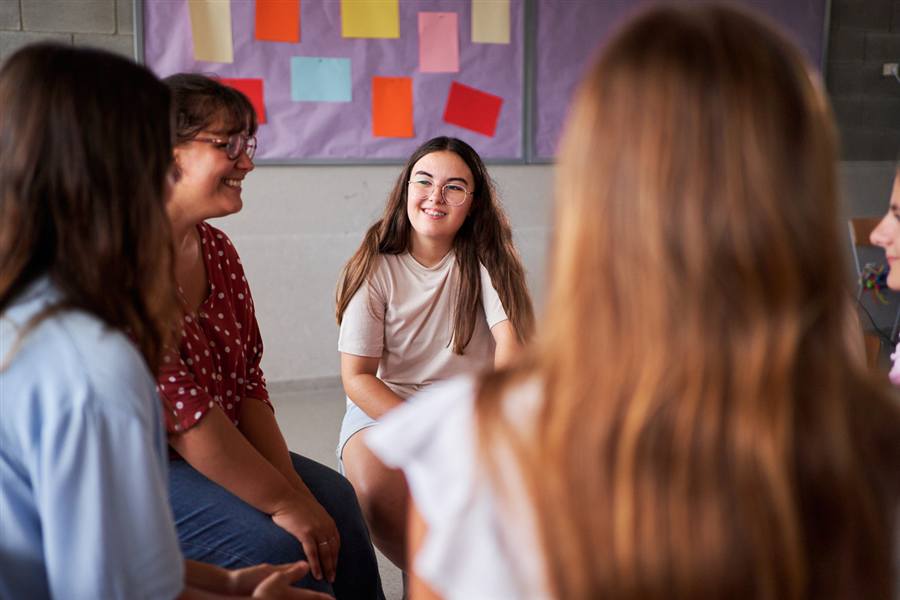 Students and a teacher in a discussion circle with idea notes on the wall